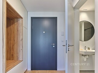 Vstupní hala s dřevěným obkladem a parketovou podlahou, moderní design, vestavěné úložné prostory a přístup do koupelny s kulatým zrcadlem.