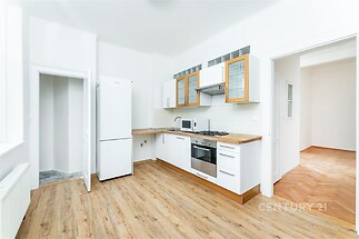 Světlá kuchyň s parketovou podlahou, moderními spotřebiči a vestavěnými skříněmi v rekonstruovaném bytě.