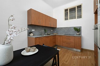 Kompaktní kuchyň s dřevěnými skříňkami, šedou pracovní deskou a parketovou podlahou, moderní styl s vestavěnými spotřebiči.