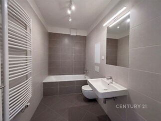 Moderní koupelna s dlažbou, velké zrcadlo, sprchová vana a topný žebřík. Světlý prostor s minimalistickým designem.