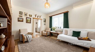 Světlý obývací pokoj s parketovou podlahou, velkými okny a pohodlným posezením, dekorativní obrazy na stěnách, stylově zařízený interiér.