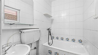 Kompaktní koupelna s bílými dlaždicemi, vanou a umyvadlem. Jednoduchý design s praktickým umístěním sanitárního vybavení.