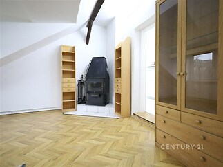 Světlý obývací pokoj s parketovou podlahou, krbová kamna v rohu, dřevěný nábytek, světlé stěny, rustikální styl, vysoké stropy.