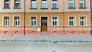 Historická fasáda bytového domu s dřevěnými dveřmi a velkými okny, udržovaná architektura a klidná lokalita poblíž centra.