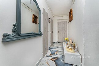 Úzká chodba s mramorovou dlažbou, zdobená zrcadlem a dekoracemi, moderní dveře a světlé stěny vytvářejí elegantní dojem.