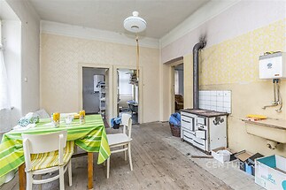 Kuchyně s dřevěnou podlahou, starým kamny a bílým obkladem. Světlý prostor nabízí možnosti rekonstrukce a modernizace.