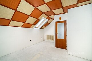 Podkrovní pokoj s dřevěným stropem a střešním oknem, bílými zdmi a jednoduchými dveřmi, vhodný pro renovaci nebo modernizaci.