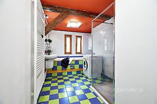 Barevná koupelna s dlažbou, sprchovým koutem a pračkou, doplněná dřevěnými trámy a moderními detaily, vytváří unikátní designový prostor.