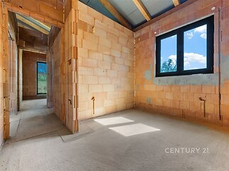 Nezařízená místnost s betonovou podlahou a velkými okny, cihlové stěny v novostavbě, moderní konstrukce.