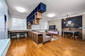 Prostorný obývací pokoj s parketovou podlahou, moderním vestavěným nábytkem a velkými okny. Elegantní otevřený koncept zajišťuje světlý interiér.