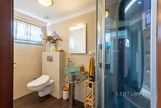 Moderní koupelna s proskleným sprchovým koutem, závěsnou toaletou a parketovou podlahou. Světlý interiér s minimalistickým zařízením.