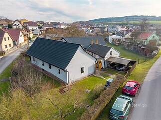 Rodinný dům s bílou fasádou, moderní střechou a prostornou zahradou, nacházející se v klidné venkovské oblasti s malebným výhledem.