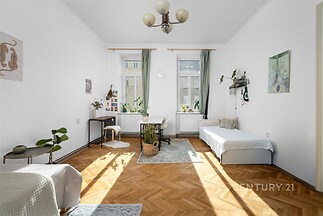 Světlý obývací pokoj s parketovou podlahou, velká okna s bílými rámy, moderní dekorace a minimalistický nábytek, ideální pro rekreační obývání.