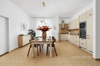 Prostorná kuchyň s dlažbou, moderními spotřebiči a velkým jídelním stolem, světlý interiér s velkými okny a elegantními skříňkami
