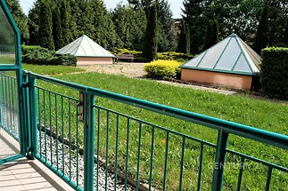 Zahrada s pečlivě upraveným trávníkem, doplněná skleníky a kovovým zábradlím, obklopená vzrostlými stromy a keři, nabízí soukromí a klid.