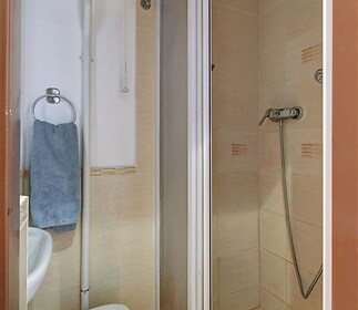 Malá koupelna s dlažbou, sprchovým koutem a moderními obklady, ideální pro menší byty nebo garsonky.