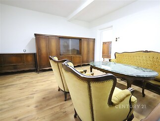 Prostorný obývací pokoj s parketovou podlahou, dřevěný nábytek v klasickém stylu, velký oválný stůl a světlé stěny vytvářejí elegantní atmosféru
