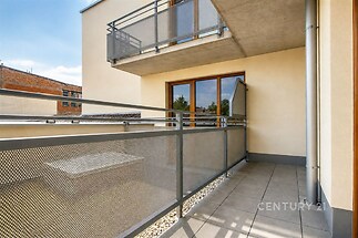 Prostorný balkón se světlou dlažbou a moderním zábradlím, zajišťující venkovní posezení s výhledem, vhodné pro slunné dny a relaxaci.