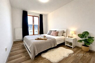 Prostorná ložnice s parketovou podlahou, velkými okny a moderním nábytkem, vytváří světlý prostor pro relaxaci.