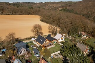 Letecký pohled na venkovský dům s terasou, zahradou a okolní přírodou. Nachází se v klidné lokalitě s výhledem na lesy a pole.