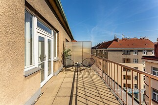 Prostorný balkon s dlažbou, moderním zábradlím a výhledem na střechy města. Poskytuje soukromí a ideální místo pro relaxaci.