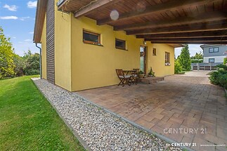 Krytá terasa s dlažbou, dřevěným stropem a posezením, obklopena upravenou zahradou, nabízí klidné místo pro relaxaci.