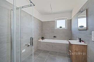 Prostorná koupelna s moderními obklady, skleněným sprchovým koutem a vestavěnou vanou, k dispozici velké okno pro přirozené světlo.