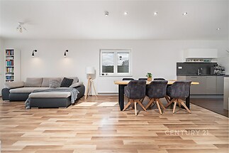 Prostorný obývací pokoj s parketovou podlahou, moderní sedačkou a velkými okny, propojený s jídelním koutem a elegantní kuchyní.