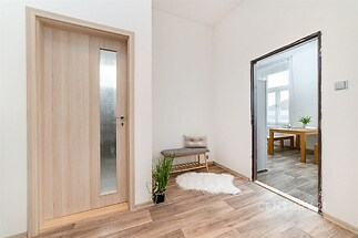 Vstupní hala s parketovou podlahou, světlým nábytkem a moderně působícími skleněnými dveřmi, které vedou do jídelny s velkými okny.