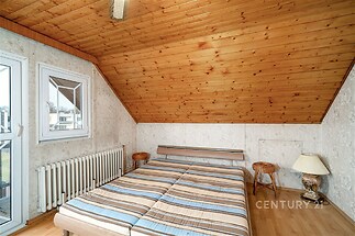 Podkrovní ložnice s dřevěným obložením a parketovou podlahou, velká okna a útulné světlo, klasický styl a klidná atmosféra.