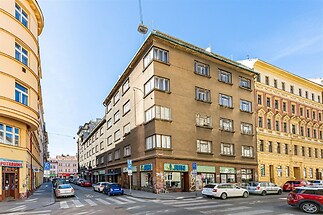 Městský činžovní dům s renovovanou fasádou, velkými okny a obchodními prostory v přízemí, nacházející se na rohu rušné ulice.