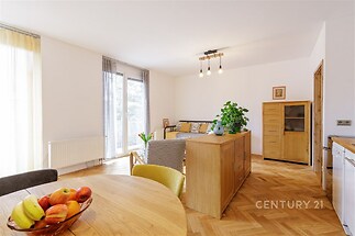 Světlý obývací pokoj s parketovou podlahou, velkými okny a moderním nábytkem.