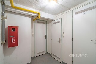 Úložný prostor se světlými stěnami, bezpečnostními dveřmi a průmyslovou betonovou podlahou, vhodný pro uskladnění v bytovém domě.