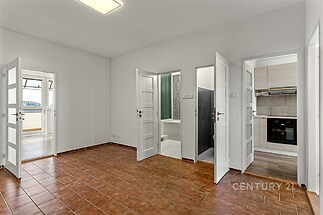 Prostorný pokoj s dlažbou a bílými dveřmi, vedoucí do moderní kuchyně a koupelny. Výborný stav a uspořádání pro rodinné bydlení.