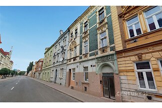 Historická ulice s řadou zrekonstruovaných domů, zdobené fasády a velká okna, ideální pro investici nebo bydlení v blízkosti centra města.