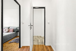 Úzká chodba s parketovou podlahou a bílými stěnami, přístup do obývacího pokoje s dřevěnými prvky a uklizeným moderním vzhledem.