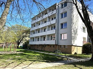 Bytový dům s moderní fasádou, velkými okny a prostornými balkony, obklopený zelení a nachází se v klidné okrajové části města.