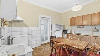 Prostorná kuchyň s dřevěným nábytkem, dlažba na stěnách a parketová podlaha, nabízí retro styl a praktické uspořádání.