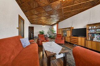Prostorný obývací pokoj s dřevěným stropem, parketovou podlahou a retro nábytkem, vybavený knihovnou a velkou pohovkou v rustikálním stylu.