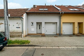 Řadový rodinný dům s moderní fasádou, garážovými vraty a novou střešní krytinou; v klidné rezidenční čtvrti s dlážděným přístupem.