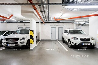 Podzemní parkovací stání s betonovou podlahou, moderními ventilačními systémy a dobrým osvětlením, vhodné pro dvě auta.