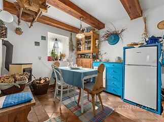 Rustikální kuchyň s dřevěnými trámy, dlažba, modrá a dřevěná kuchyňská linka, kamna na dřevo, útulný venkovský styl.