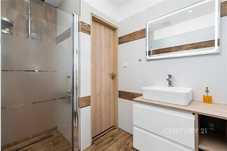 Moderní koupelna s keramickými dlaždicemi, proskleným sprchovým koutem a stylovým osvětleným zrcadlem, nabízí elegantní design a funkčnost.