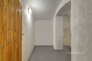 Chodba se zděnými stěnami a betonovou podlahou, osvětlená nástěnným světlem, nabízí možnost úložného prostoru nebo přístupu do dalších místností.