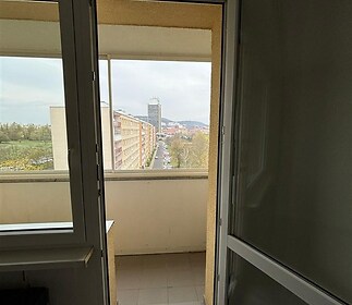 Otevřený balkon s dlažbou, výhledem na město a moderními dveřmi, ideální pro relaxaci a užívání panoramatu.