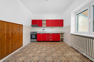 Kuchyň s dlažbou, moderní červené skříňky, prostorná dispozice, velké okno, dobré světlo, vhodná pro renovaci.