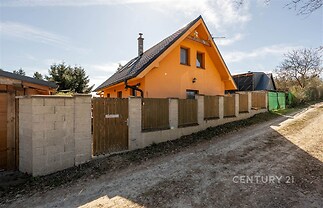 Rodinný dům se sedlovou střechou, oplocený pozemek s dřevěným a betonovým plotem, udržovaná fasáda, klidná lokalita.