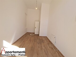 Světlý pokoj s parketovou podlahou, vysokým stropem a bílými stěnami. Jednoduché osvětlení a minimalistický styl nabízejí moderní design.