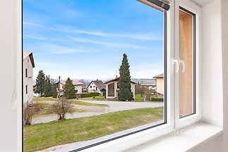 Výhled z okna na klidnou rezidenční čtvrť s velkými okny, která zajišťují dostatek přirozeného světla, a moderním plastovým rámem.