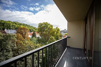Prostorný balkon s dlažbou, nabízející výhled na zelené okolí, ideální pro relaxaci. Skleněné zábradlí zajišťuje bezpečnost a moderní vzhled.